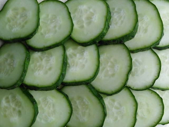Several slices of cucumber are arranged in an overlapping pattern. The cucumber slices show a vibrant green outer skin and a pale, watery interior with visible seeds.