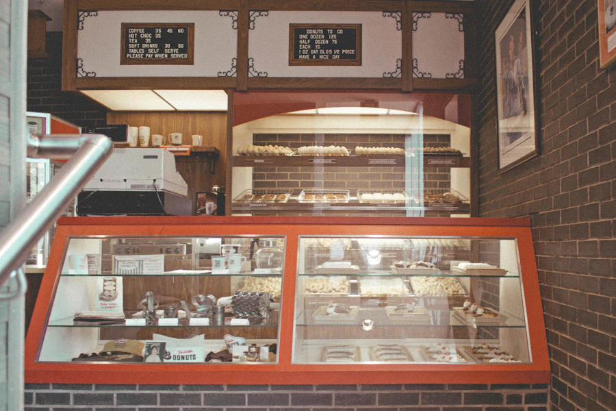 An old shop display case with a painted orange frame and a lit glass front, hand-lettered signs pinned on the brick above it.