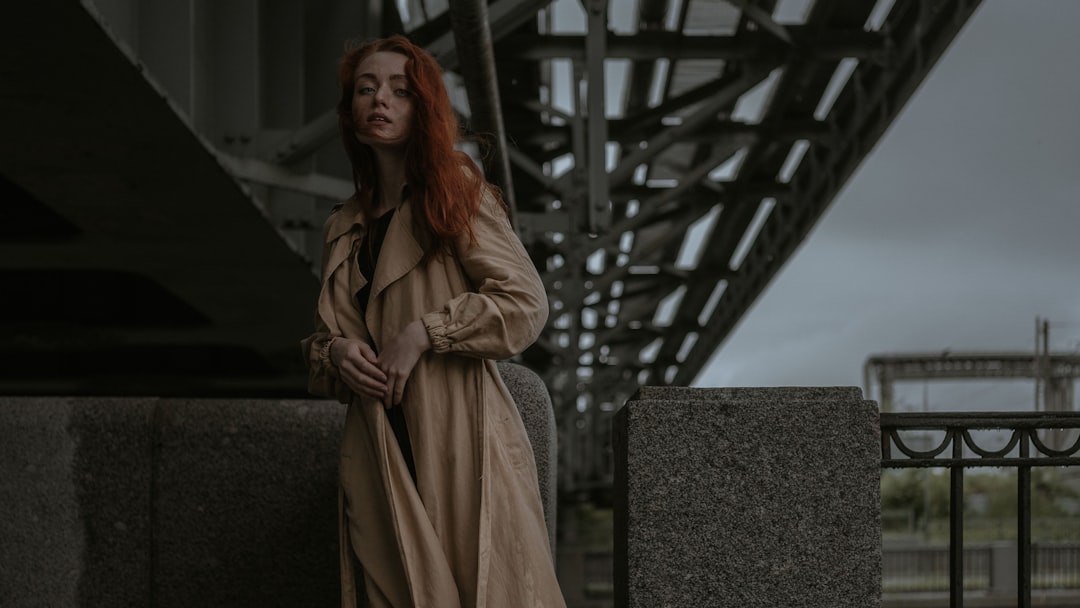 woman in brown coat standing near gray concrete wall during daytime