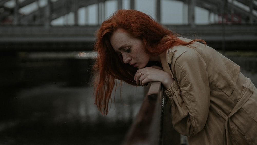 woman in brown coat leaning on brown wooden fence