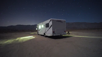 A rugged van parked at sunset on a desert plateau with a lone male traveler sitting on the hood.