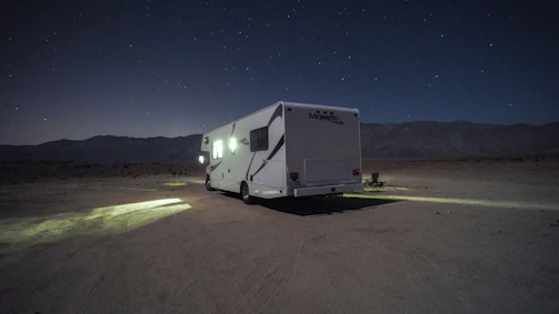 A rugged van parked at sunset on a desert ridge with a lone male traveler setting up camp.
