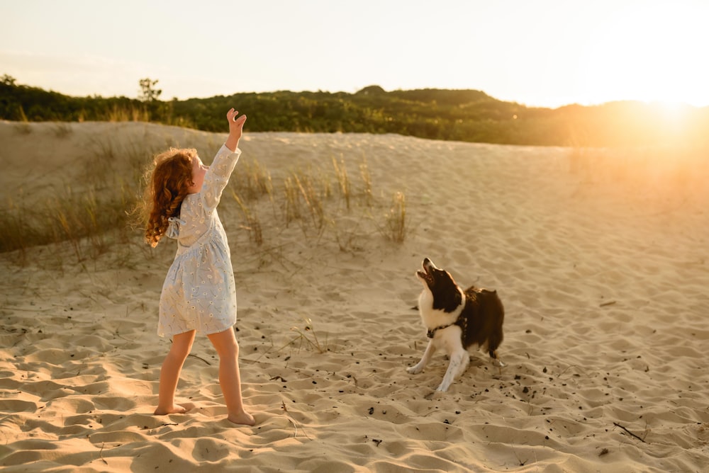 woman in white dress walking on beach with black and white short coat dog during daytime