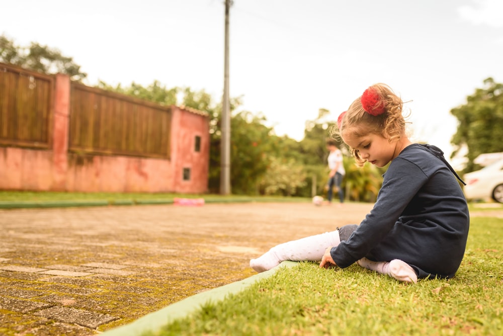 boy in black jacket and white pants sitting on green grass field during daytime