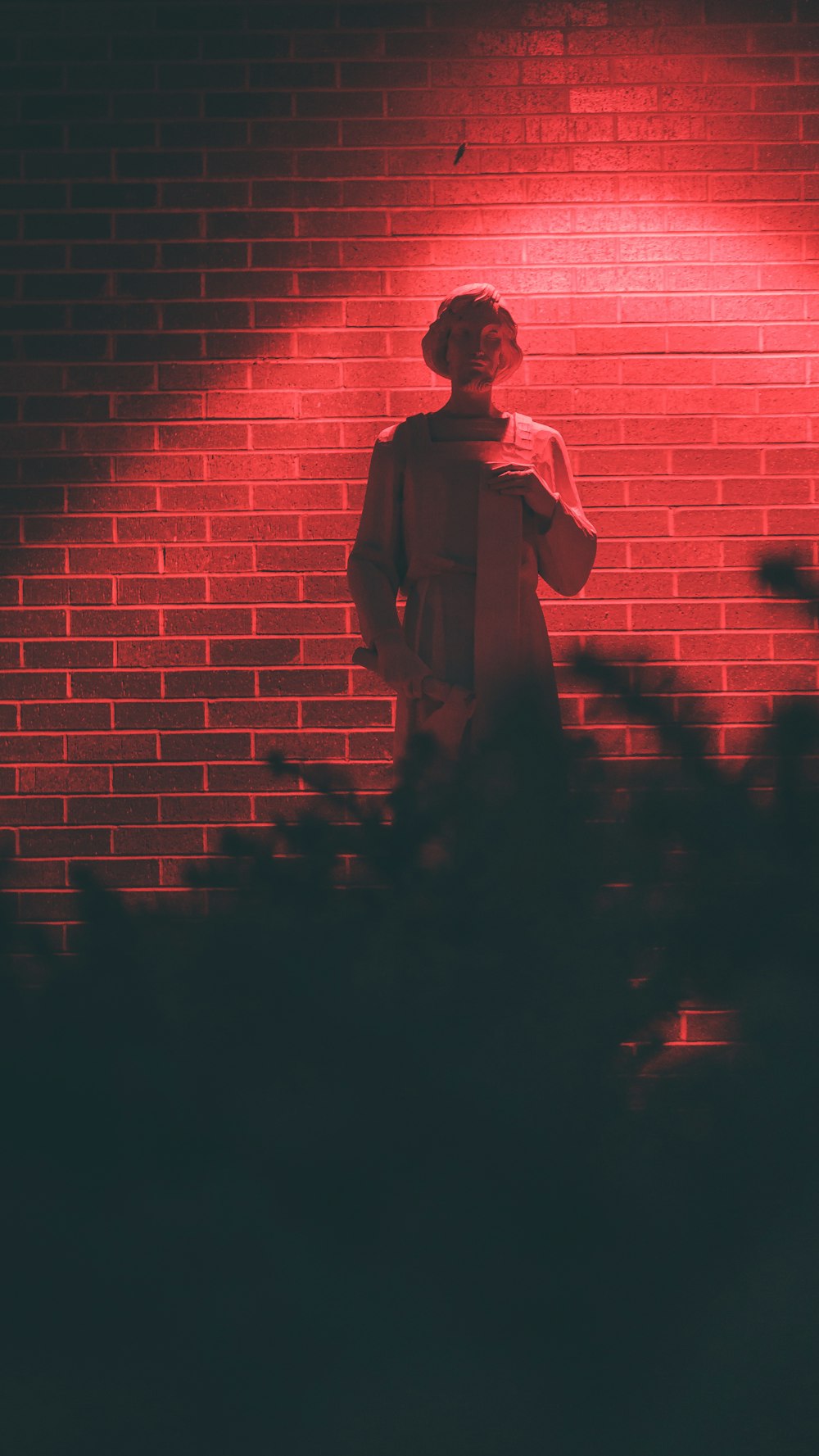 man in brown shirt standing beside brick wall