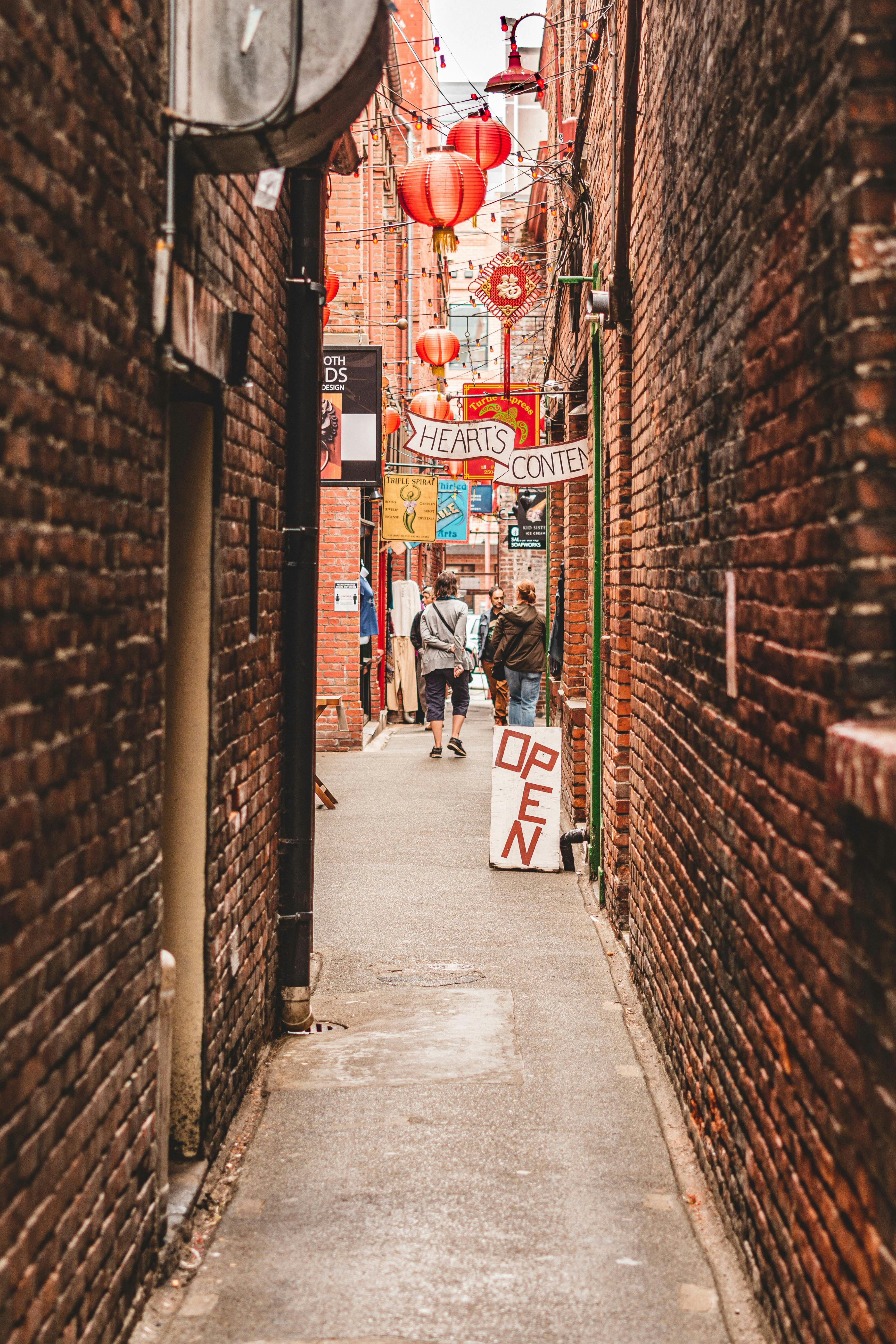 A narrow cobblestone alleyway with people walking, flanked by brick walls and buildings on either side.