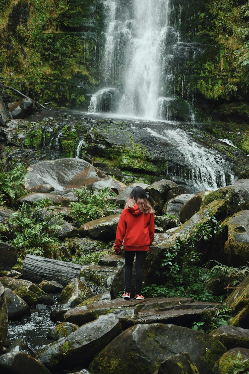 woman in red jacket standing near waterfalls during daytime
