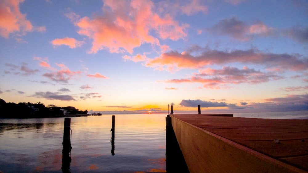 brown wooden dock on body of water during sunset