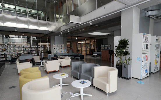 Cozy reading lounge with comfortable chairs, soft lighting, and fans in a modern library setting.