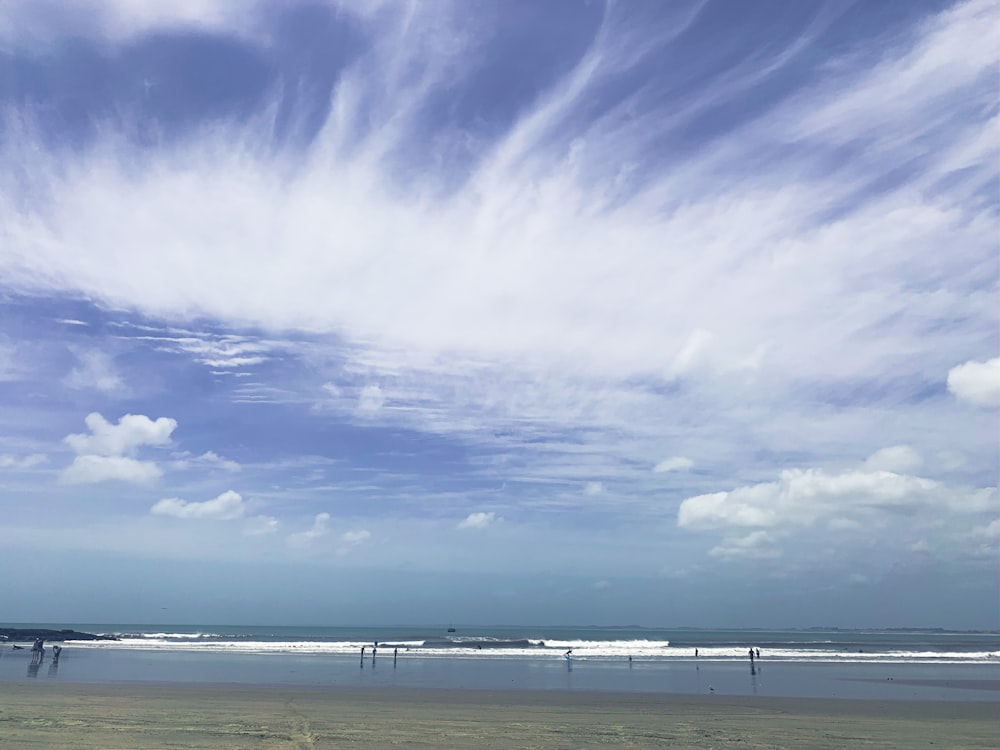 people walking on beach under blue sky and white clouds during daytime