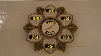 A decorative wall clock with a flower-like pattern, featuring multiple digital time displays and a central analog display showing a date. The frame has intricate designs with leaf shapes surrounding the displays, presenting a blend of modern digital and traditional decorative elements.