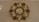 A decorative wall clock with a flower-like pattern, featuring multiple digital time displays and a central analog display showing a date. The frame has intricate designs with leaf shapes surrounding the displays, presenting a blend of modern digital and traditional decorative elements.