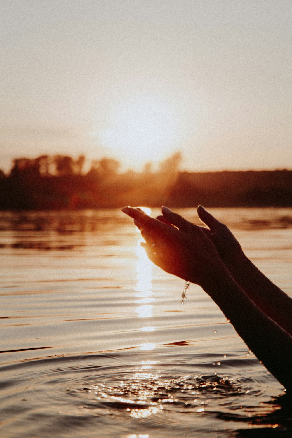 persons hand on water during sunset