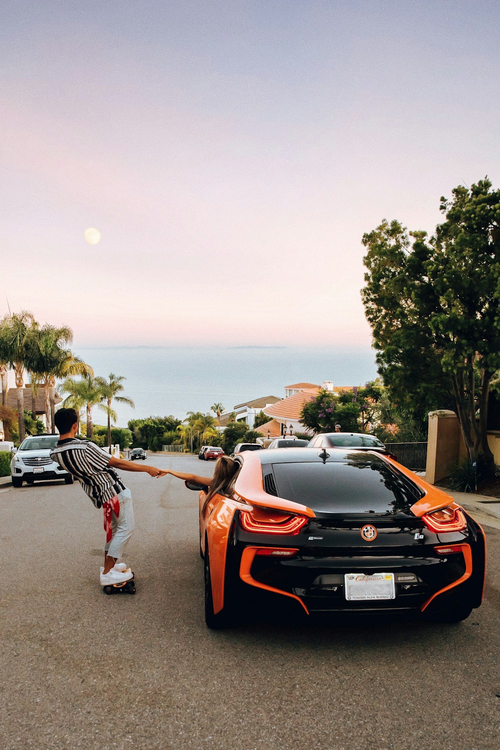 man in black and white stripe shirt and black pants standing beside orange and black car