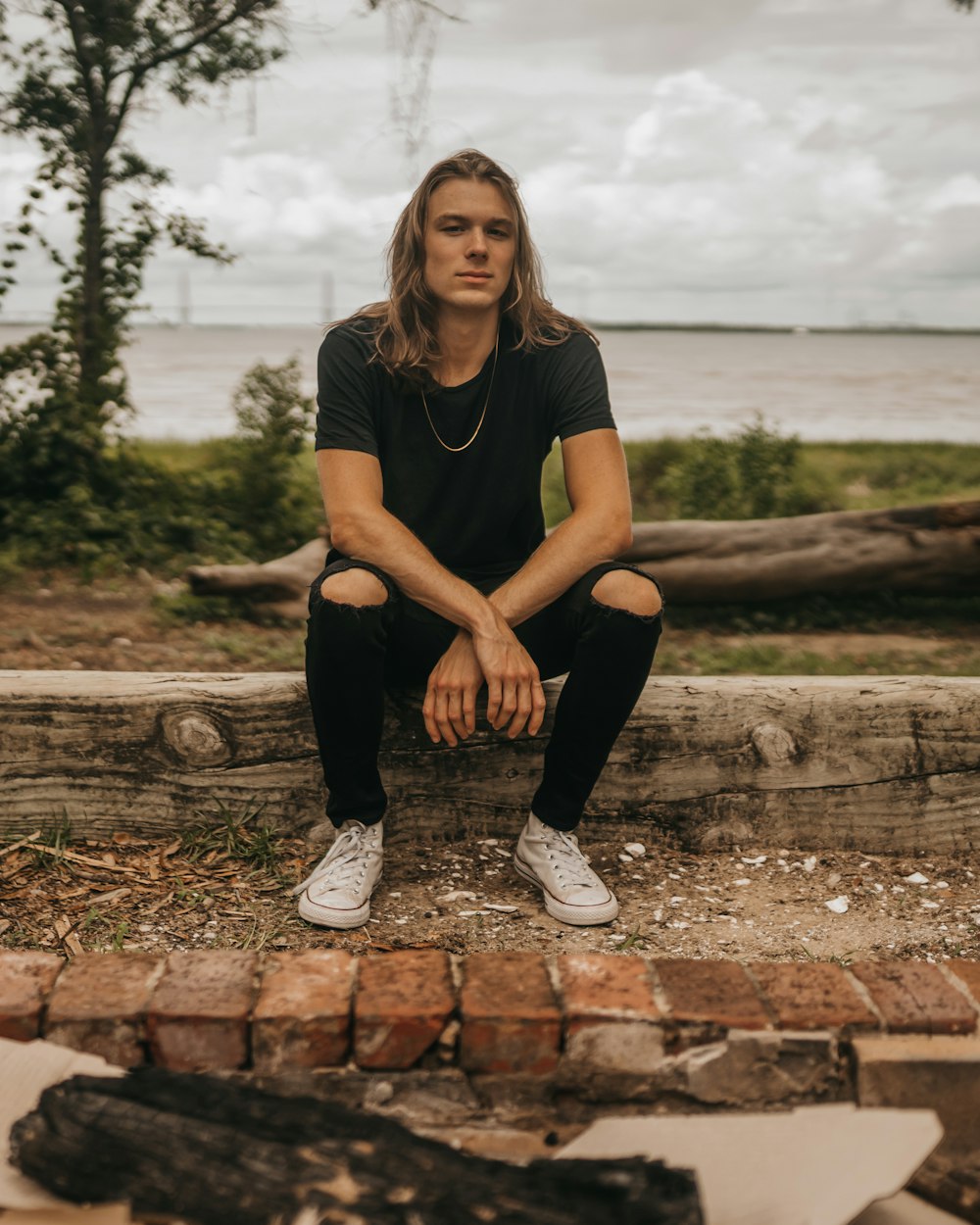 woman in black crew neck t-shirt and black pants sitting on brown wooden fence during