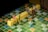 Miniature figurines are positioned on a Scrabble board, with yellow tile stacks spelling out 'NO L...ING'. The scene appears playful and imaginative, as the miniatures mimic real-life interactions in a board game setting.