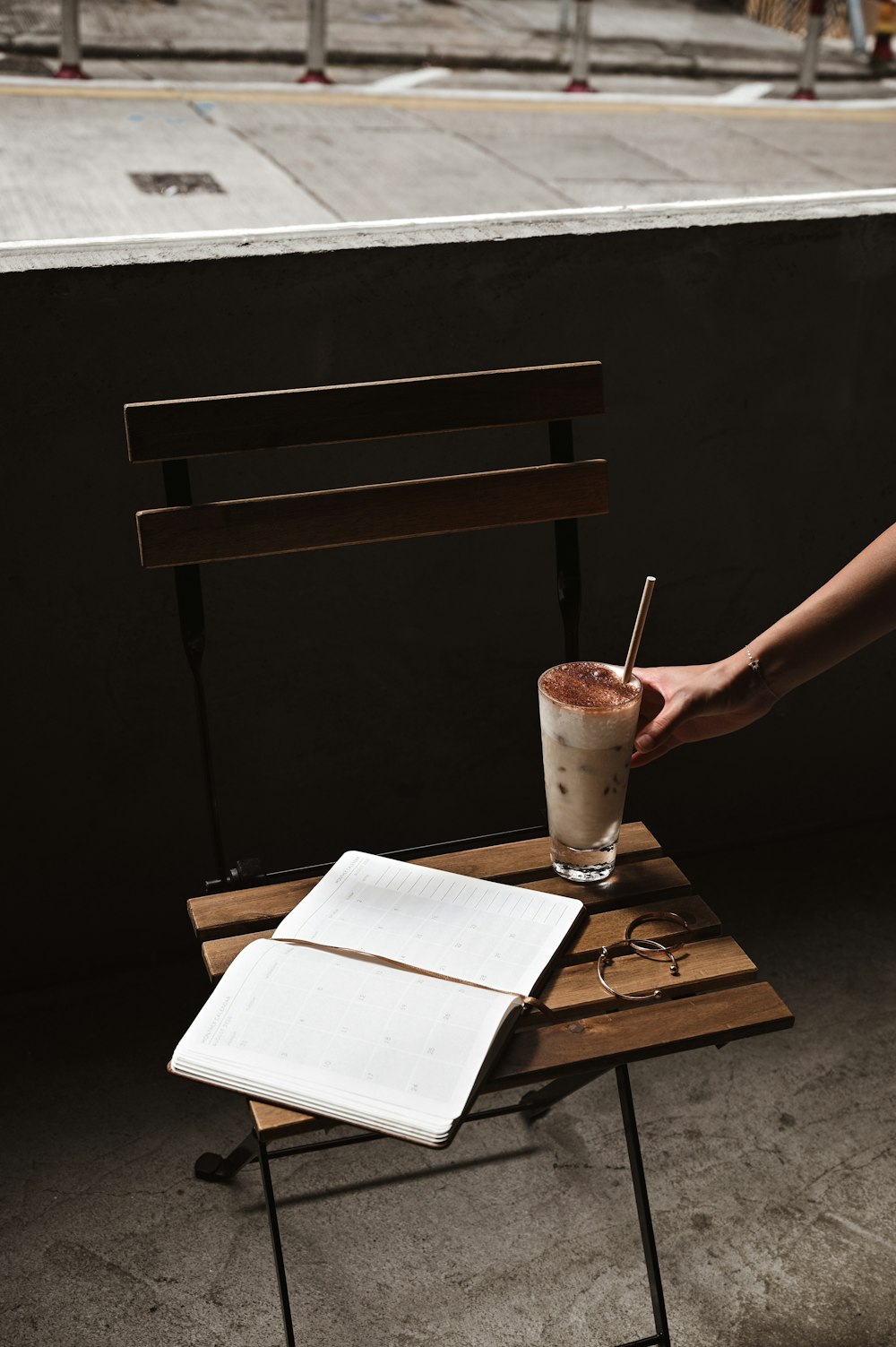 person holding clear drinking glass with brown liquid and ice