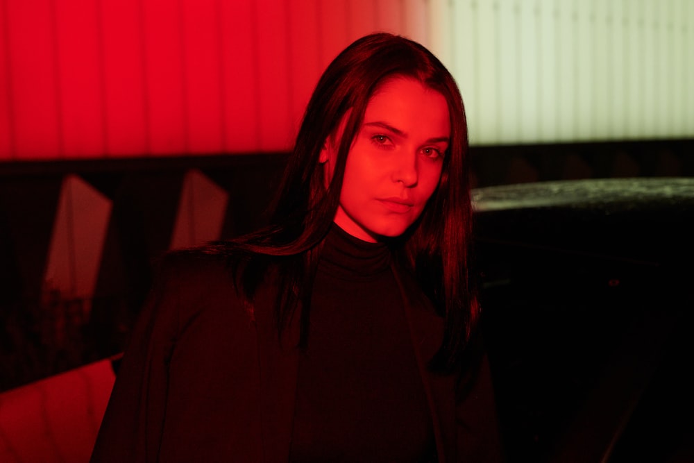 woman in black coat standing near white window blinds