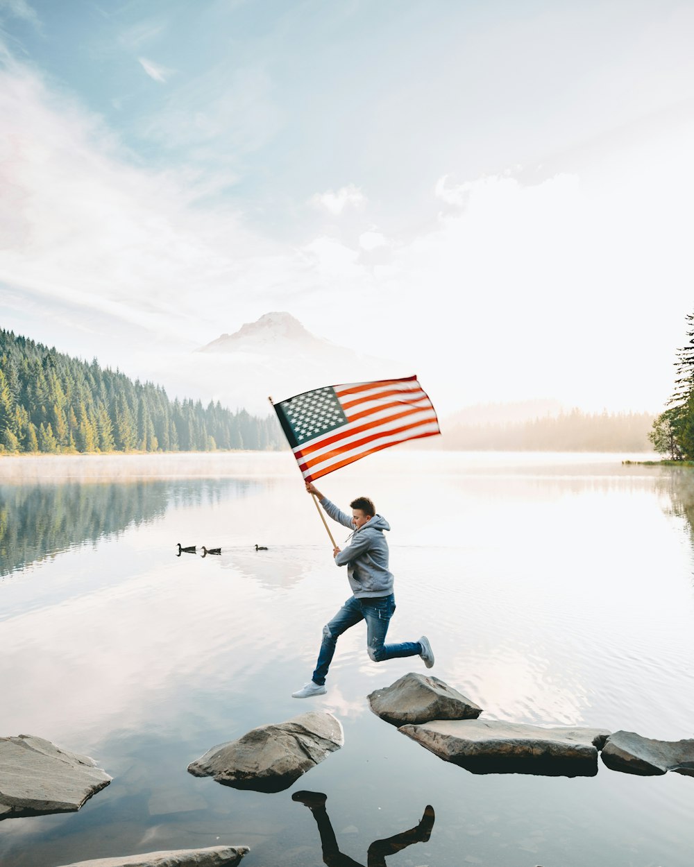 persona que nos sostiene una bandera de pie en la roca cerca del lago durante el día