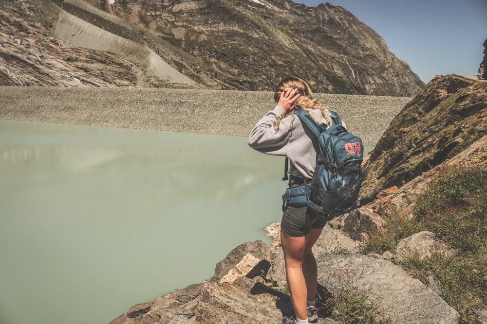 woman in black leather jacket and black backpack standing on rock formation near lake during daytime