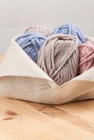 Close-up of colorful yarn balls nestled inside a rustic basket on a wooden floor.