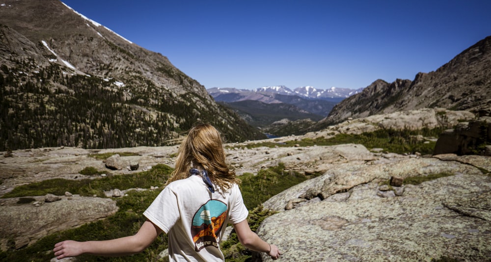 woman in white t-shirt and blue denim shorts standing on rocky ground during daytime