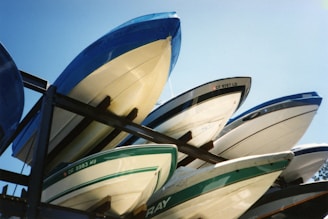 A stack of several speedboats are stored on metal racks under a clear blue sky. The boats are positioned upside down, showing their hulls which have different colors and markings.