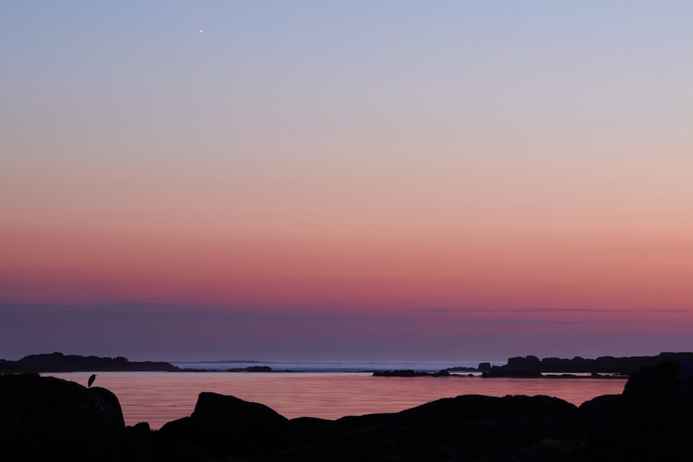 silhouette of mountain near body of water during sunset