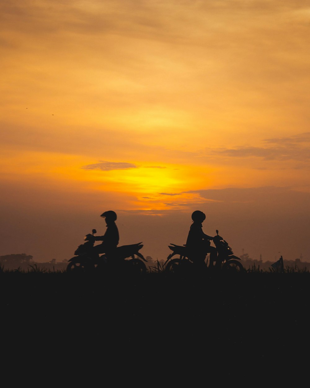 silhouette of 2 person sitting on grass during sunset