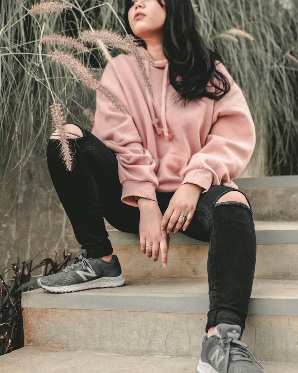woman in pink jacket and black pants sitting on concrete bench