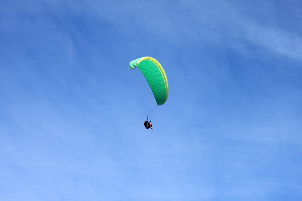 낮에는 푸른 하늘 아래 검은 색과 녹색 낙하산을 입은 사람
