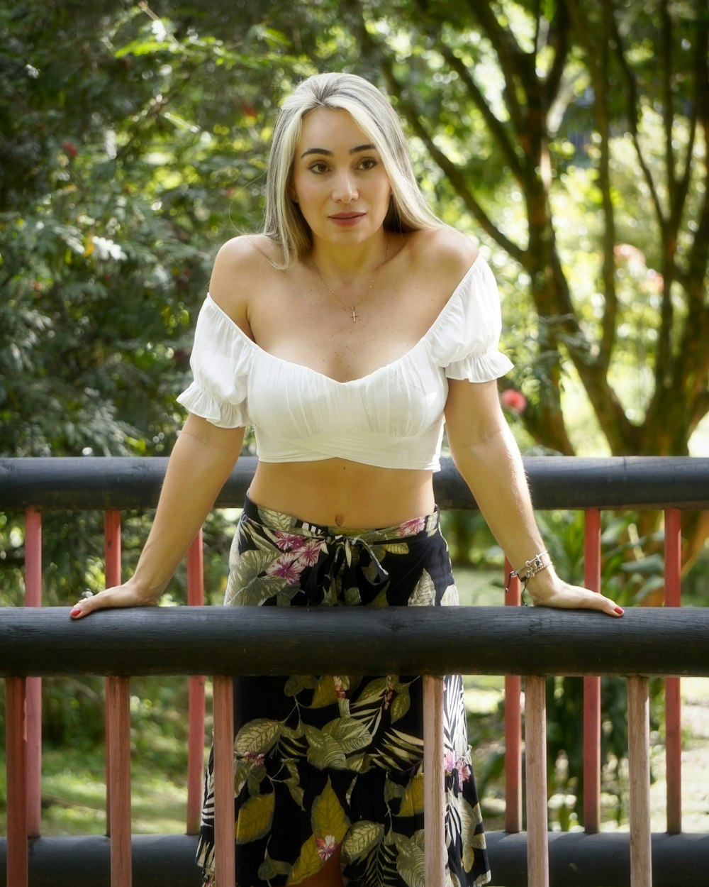 woman in white crop top and black floral skirt standing on brown wooden bridge during daytime