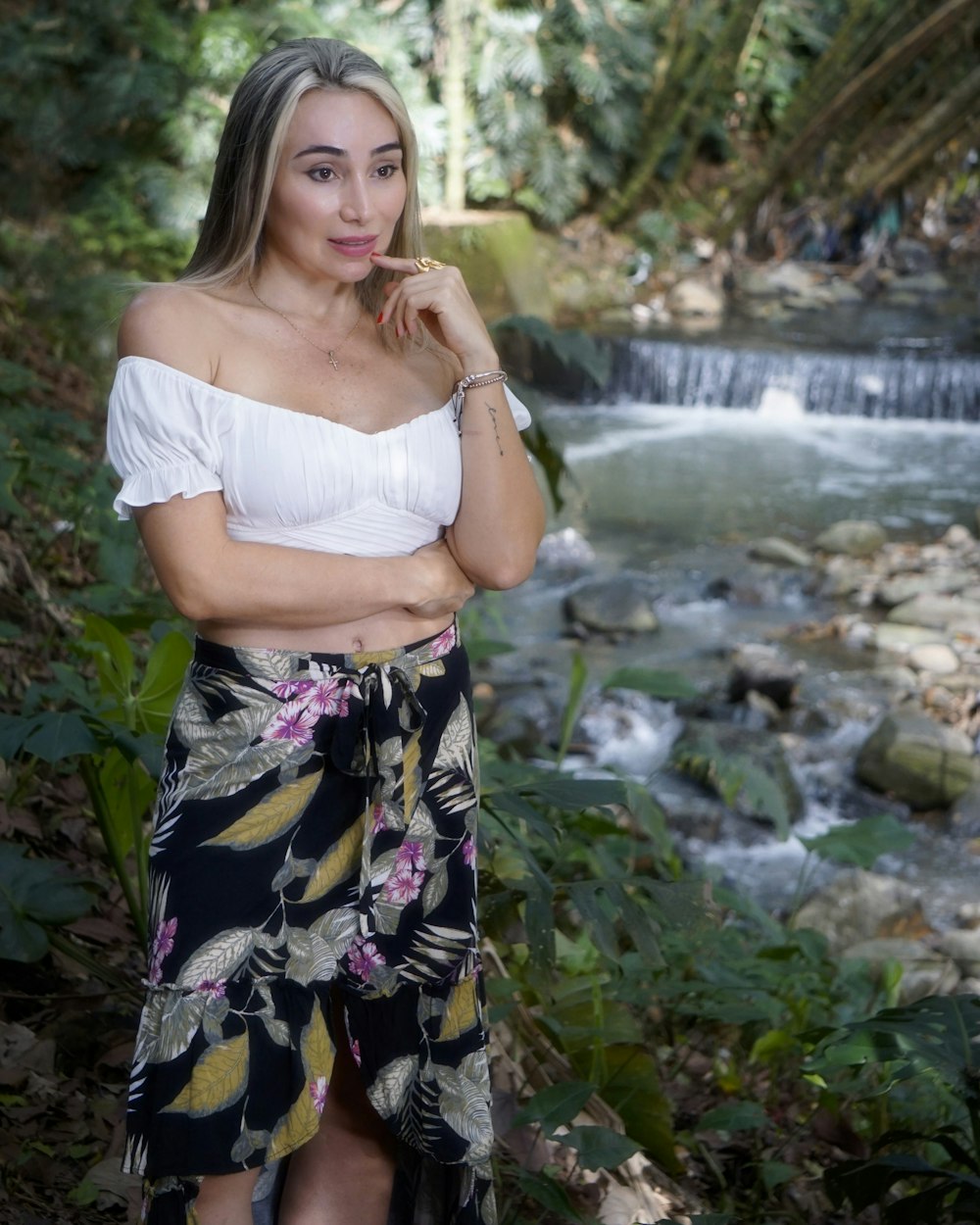 woman in white crop top and purple white floral skirt standing on rocky ground