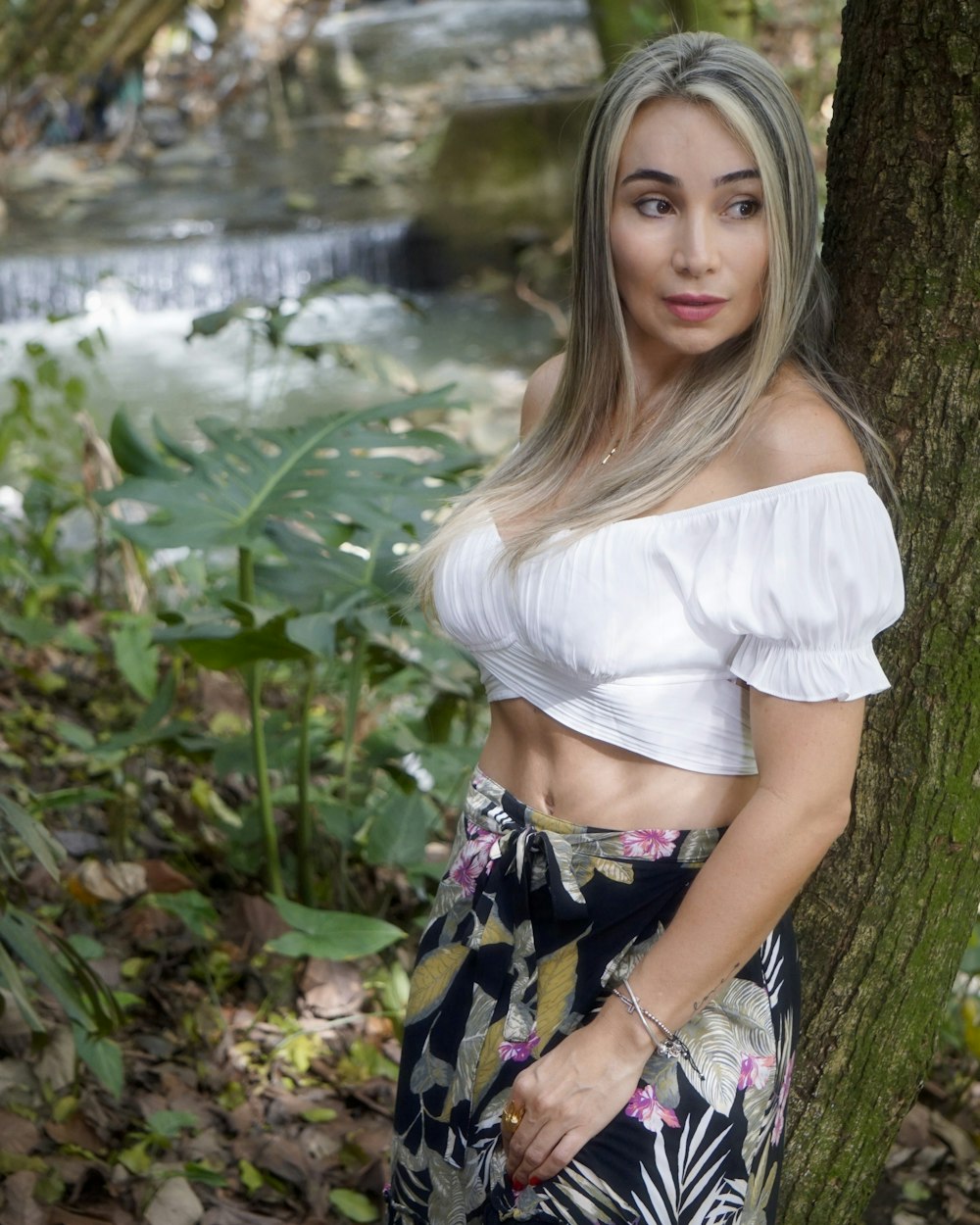 woman in white shirt and floral skirt sitting on rock near river during daytime