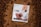 A white package labeled 'CTRL A Meal Replacement' with the flavor 'Cocoa Crunch' is placed on a bed of cocoa powder. The package design features images of cereal pieces and milk splashes. Surrounding the package are round, chocolate-colored cereal pieces.