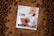 A white package labeled 'CTRL A Meal Replacement' with the flavor 'Cocoa Crunch' is placed on a bed of cocoa powder. The package design features images of cereal pieces and milk splashes. Surrounding the package are round, chocolate-colored cereal pieces.