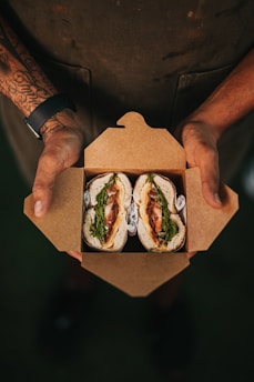 A friendly staff member handing over a neatly packed lunch box to a happy customer.