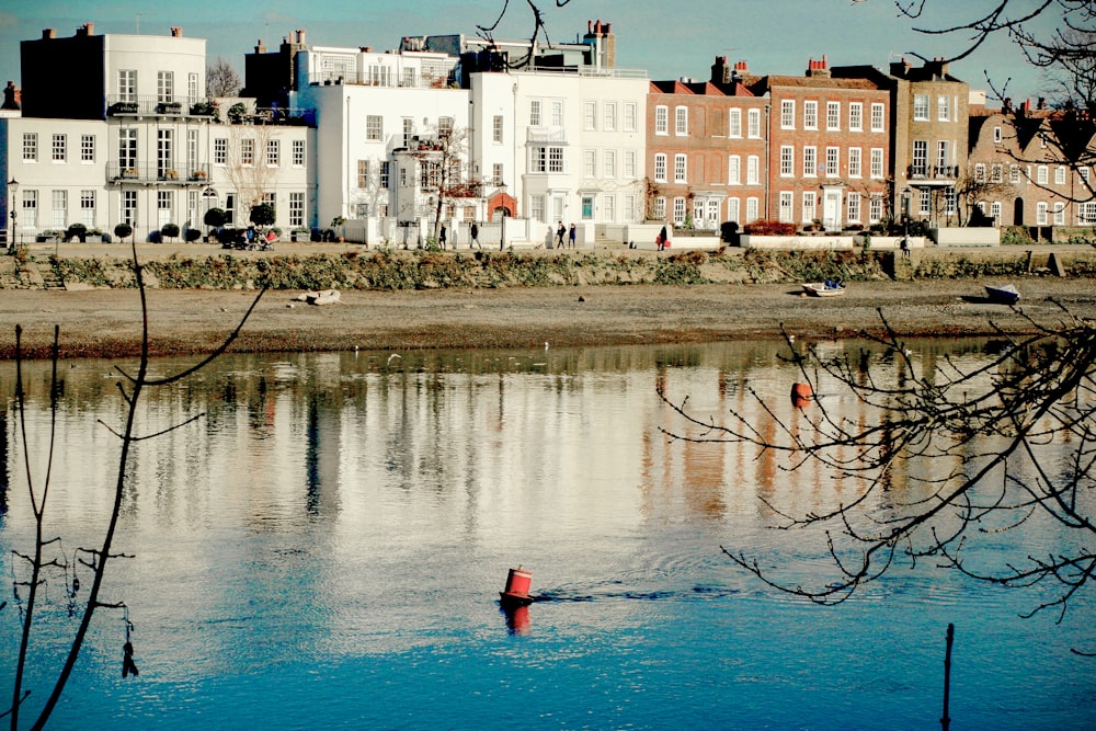 personne en veste rouge debout sur l’eau bleue près d’un bâtiment en béton blanc pendant la journée