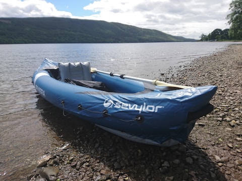 Close-up of a bright inflatable kayak resting on a rocky lakeside beach.