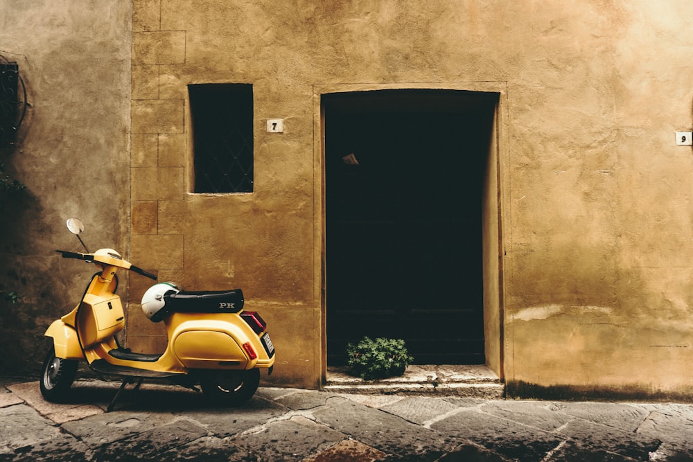 yellow and black motor scooter parked beside brown concrete building during daytime