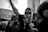 A group of people at a protest. One person in the center is passionately speaking into a microphone while raising one arm. Another person holds a sign that reads 'NO JUSTICE NO PEACE BLACK LIVES MATTER' in the background. The people display emotions of determination and solidarity.