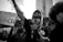 A group of people at a protest. One person in the center is passionately speaking into a microphone while raising one arm. Another person holds a sign that reads 'NO JUSTICE NO PEACE BLACK LIVES MATTER' in the background. The people display emotions of determination and solidarity.