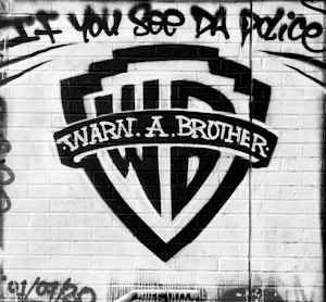 Graffiti art featuring a creative parody of a popular media company logo, with the words 'Warn a Brother' written prominently. The message 'If you see da police' is spray-painted above on a brick wall.