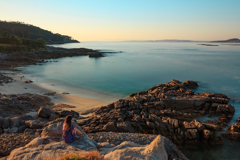 woman in blue and red dress sitting on rock near body of water during daytime