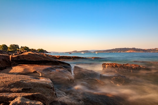 brown rocky shore under blue sky during daytime in Ría de Aldán Spain