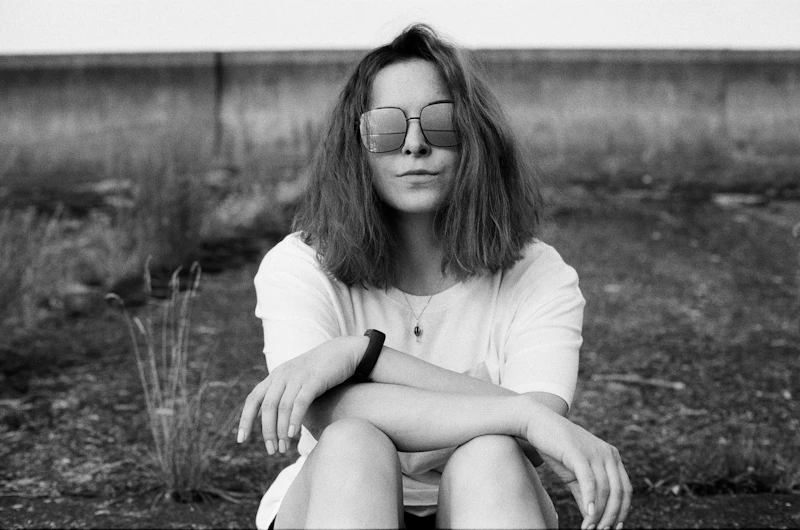 Woman in a white shirt and black shorts wearing sunglasses, sitting on the ground