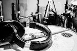 A monochrome image featuring a drum set with a focus on a pair of headphones resting on a snare drum. Drumsticks are laid across the drum, and several microphones are positioned around the set for recording. Visible branding includes 'LA Special' on the drumsticks and 'Mapex' on the drum.