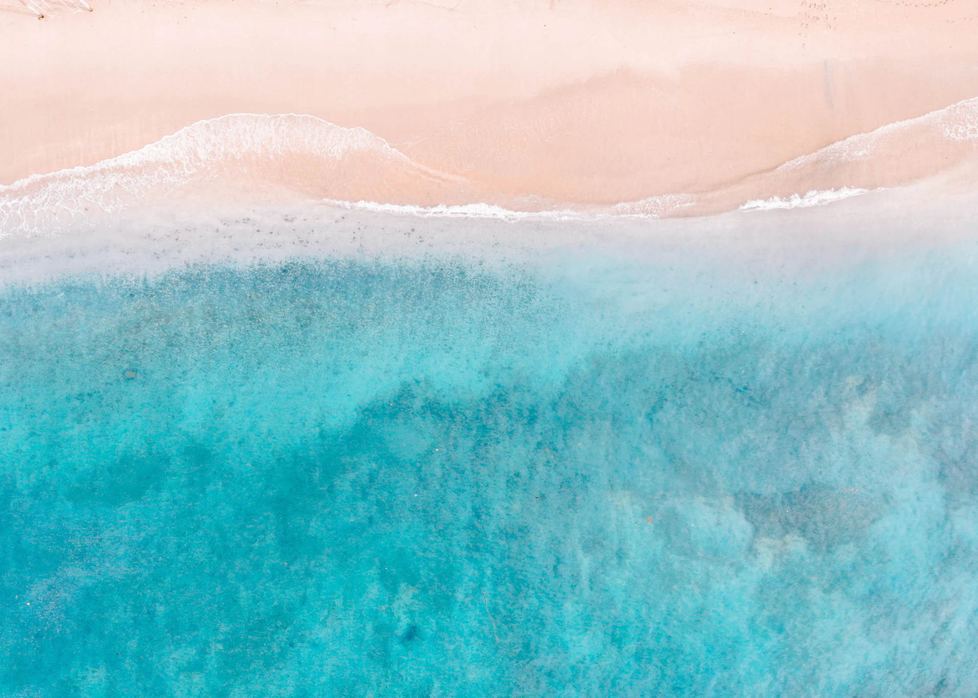 Aerial view of turquoise waves washing onto a sandy beach