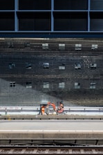 Workers in bright orange safety gear installing physical barriers along a German railway track with regional trains in the background
