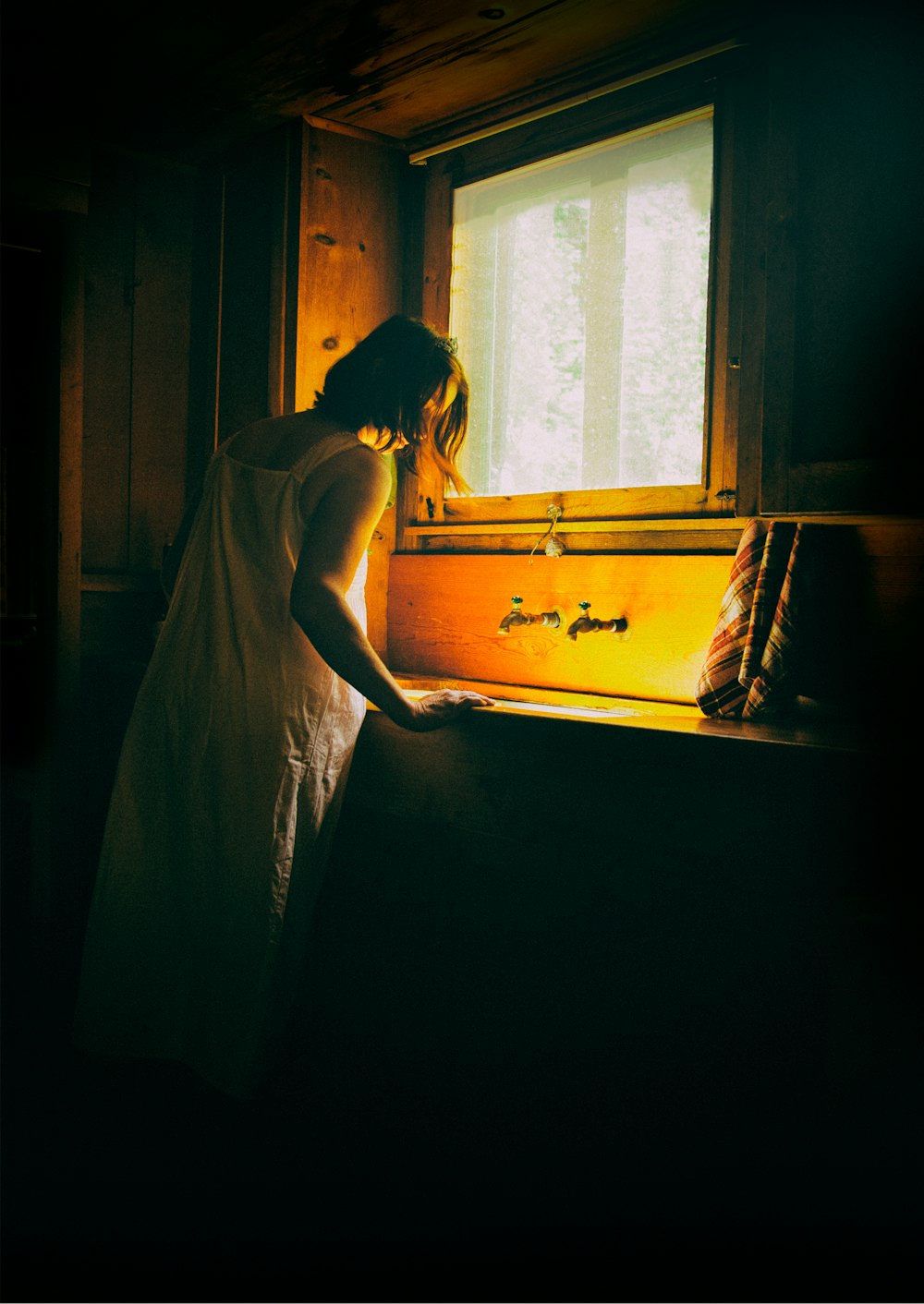 Frau im weißen Kleid steht am Fenster